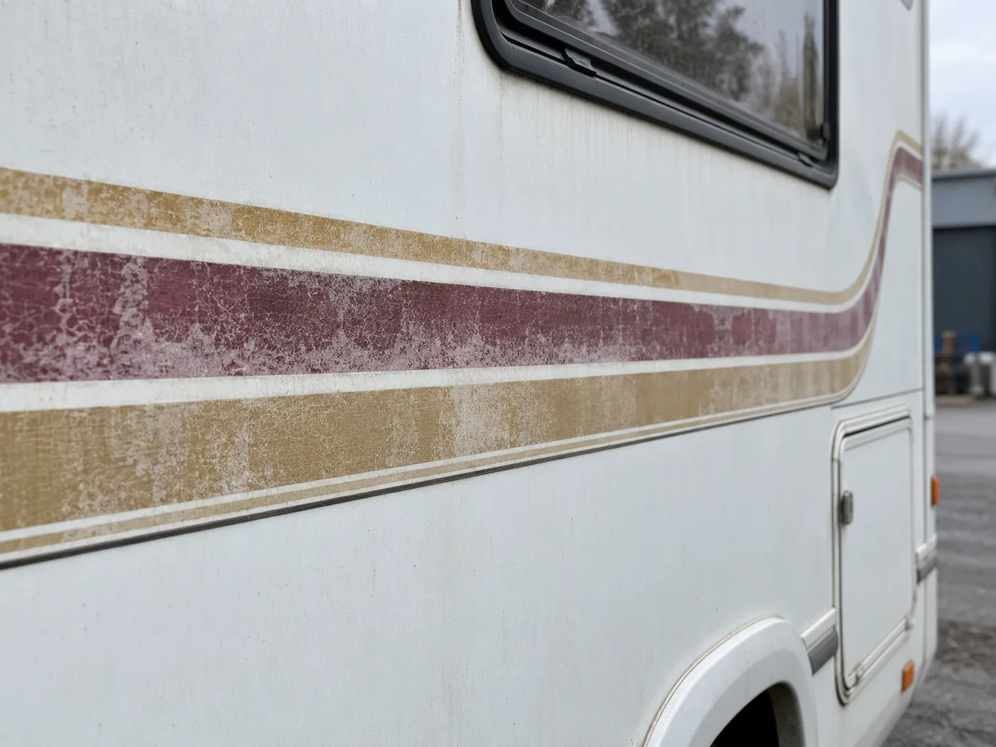 Verkleurde en verweerde sierstriping op de zijwand van een witte camper