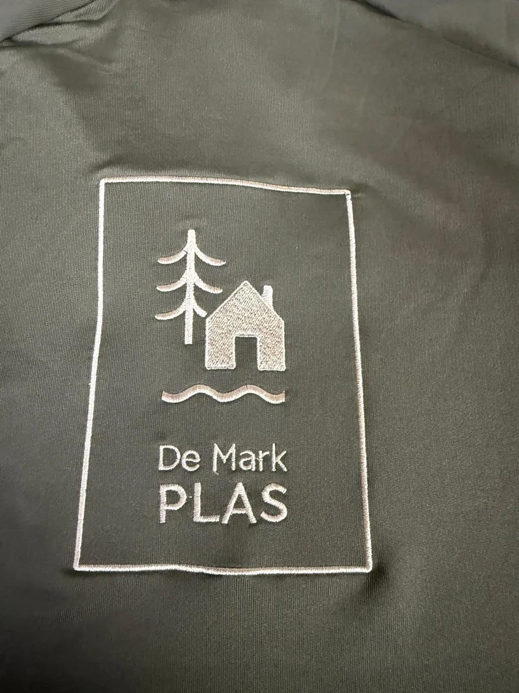 Detail van geborduurd logo op bedrijfskleding van De Markplas