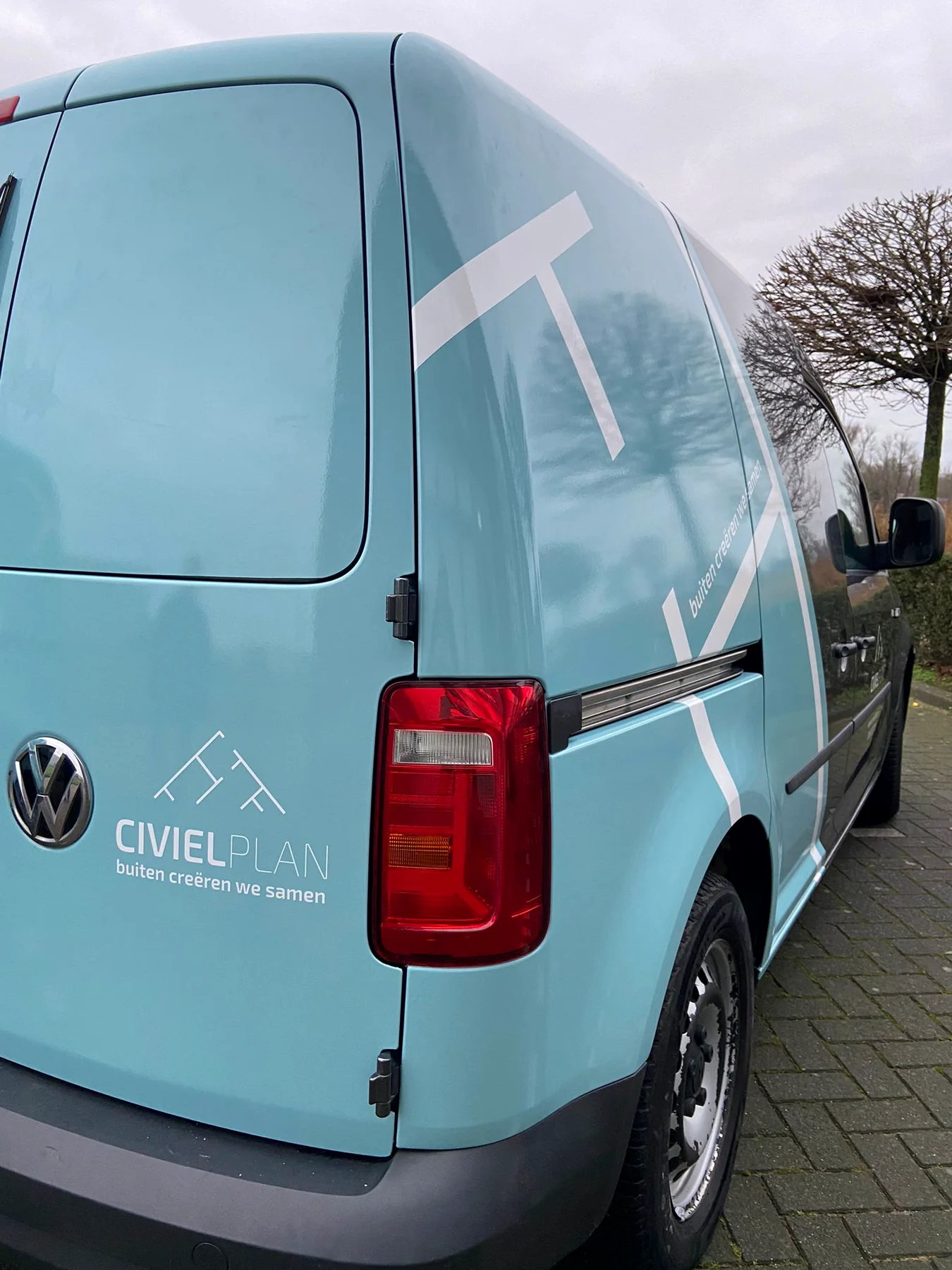 Achterzijde van een lichtblauw en antraciet beletterde Civielplan-bestelwagen