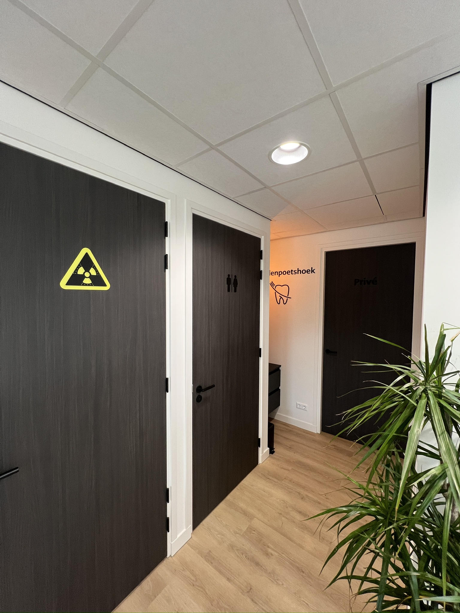 Gang in een tandartspraktijk met freesletters en pictogrammen op donkere deuren