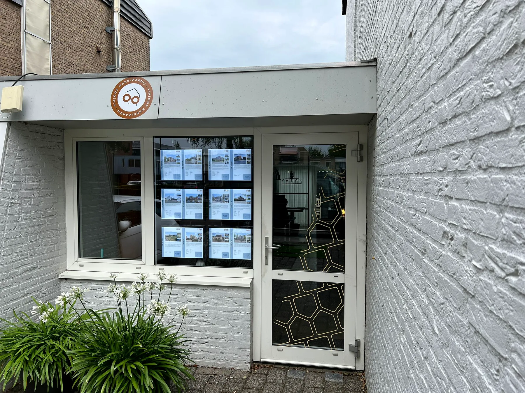 Compacte entree van Via Joop Makelaardij met rond gevelbord en raampresentatie
