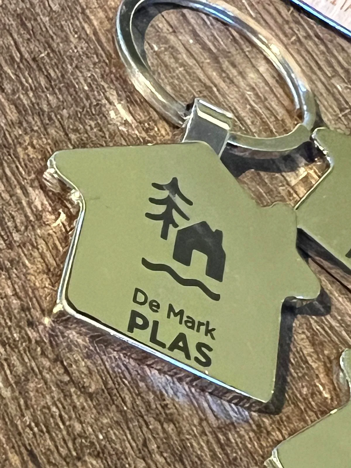 Close-up van een metalen sleutelhanger met het gegraveerde logo van De Mark Plas