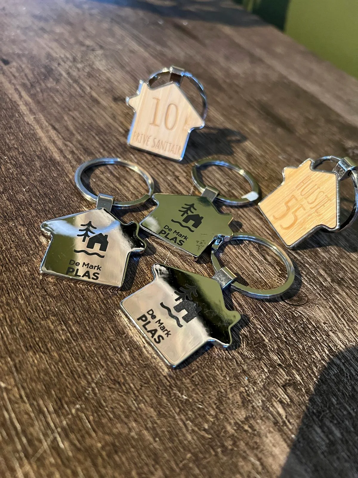 Serie huisvormige sleutelhangers met logo en huisnummers in hout en metaal