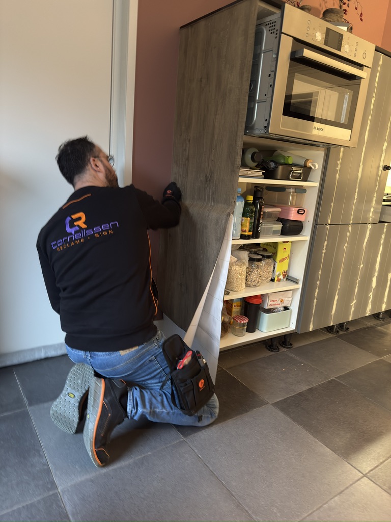 Montage van houtlookfolie op de zijkant van een hoge keukenkast