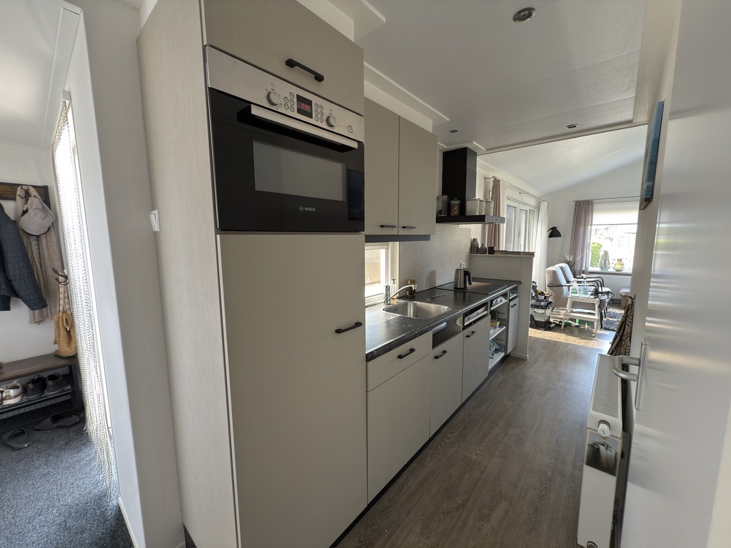 Lichte houtlook keuken met zwarte handgrepen vanuit de doorgang