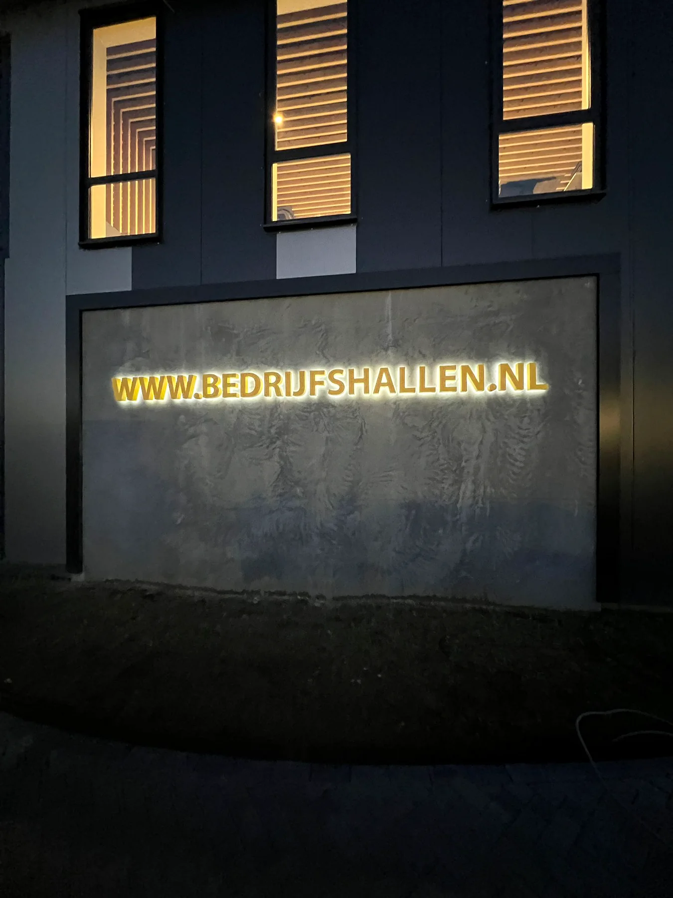 Verlichte gevelreclame van Bedrijfshallen.nl in de avond