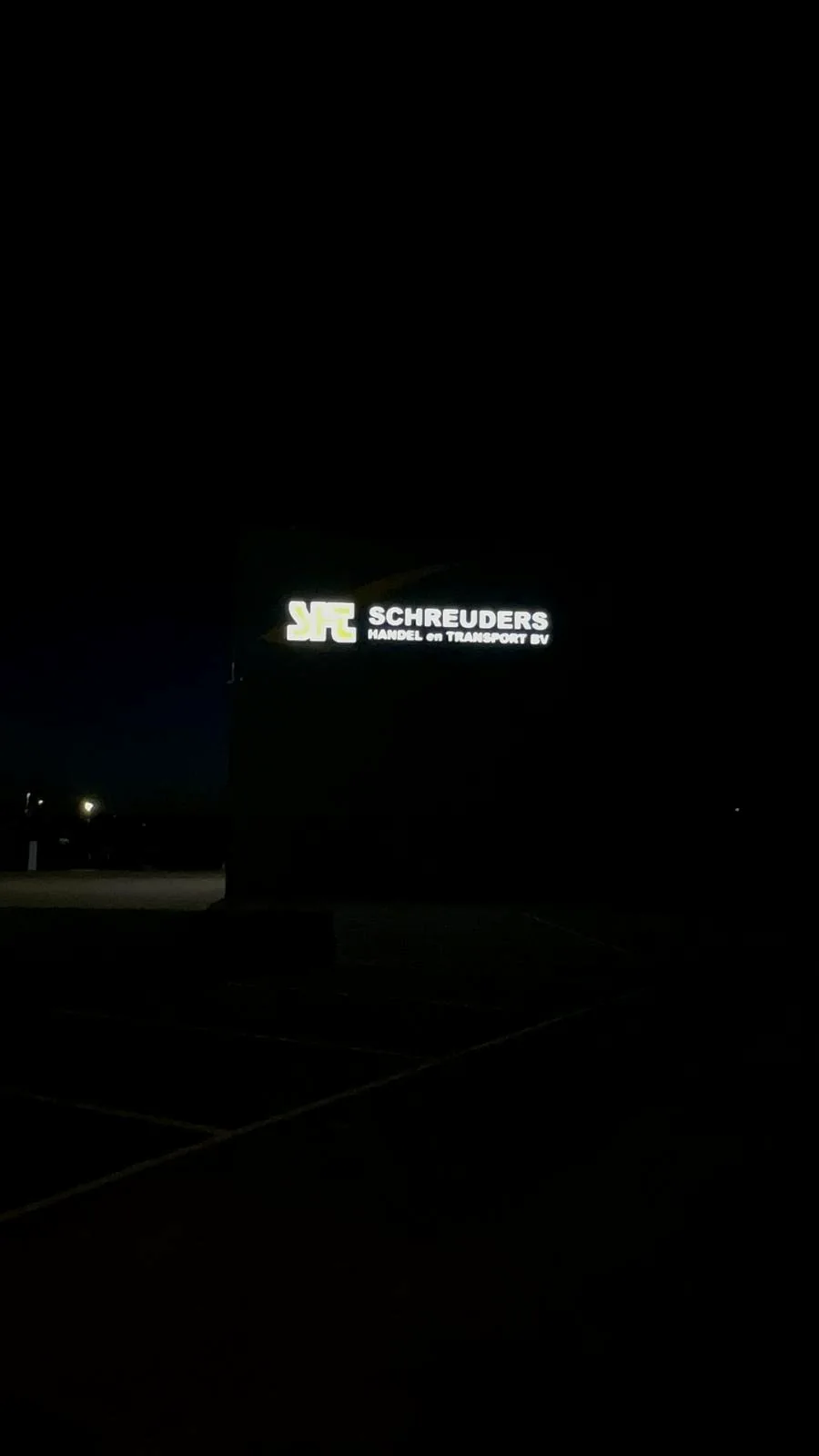 Verlichte gevelreclame van Schreuders gezien vanaf grote afstand in de nacht