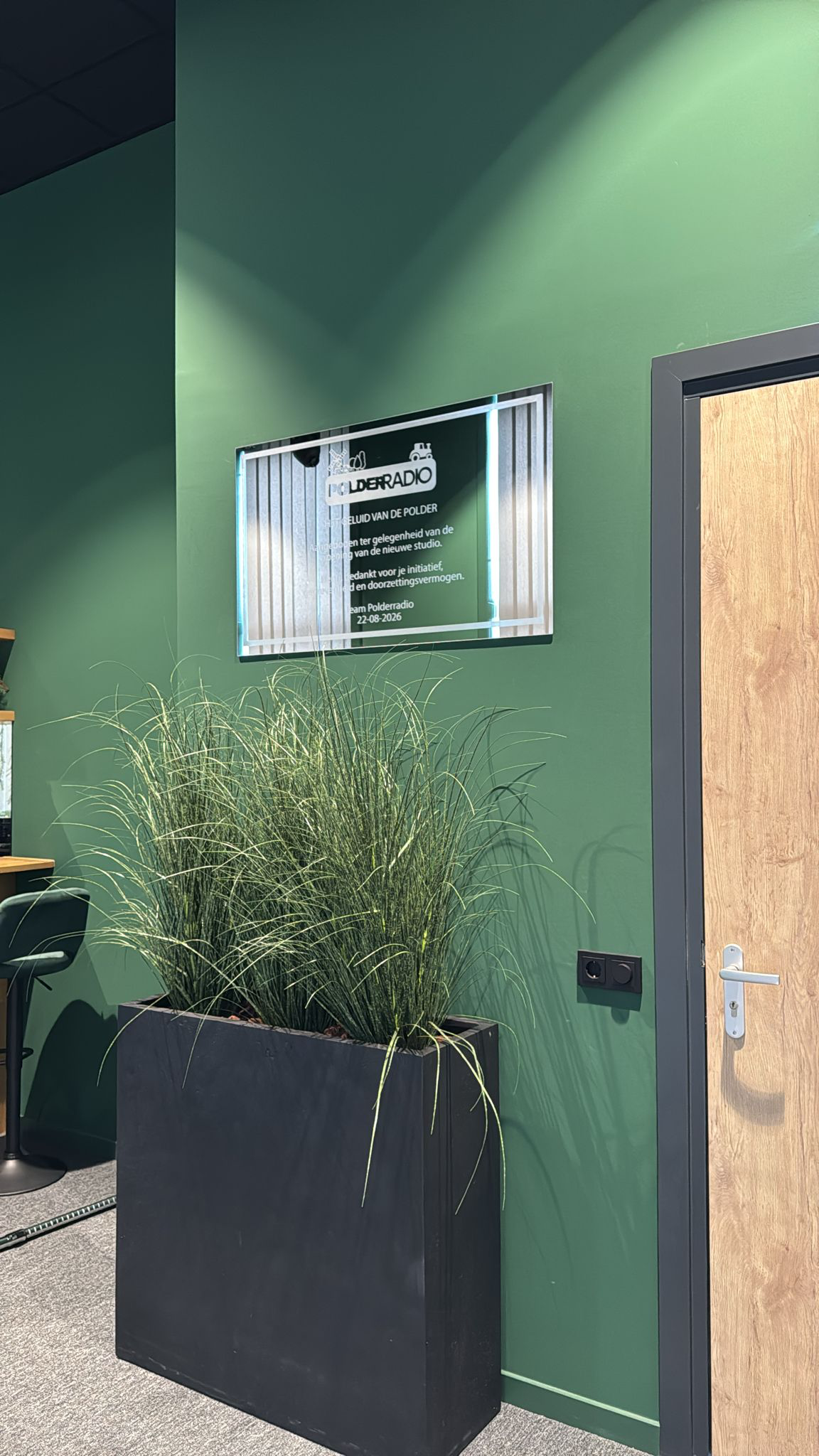 Gegraveerde acrylaatplaat voor Polderradio gemonteerd op een groene wand