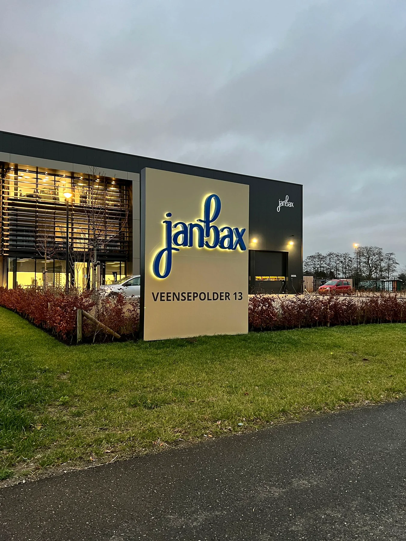 Verlichte reclamezuil van Jan Bax met gevelreclame in de schemering
