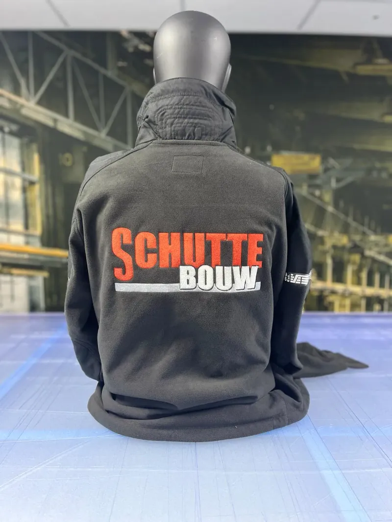 Zwarte werkjas van Schutte Bouw met grote oranje-witte borduring