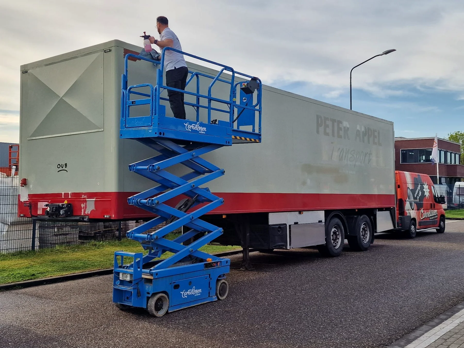 Reiniging van de bovenzijde van de trailer vanaf een blauwe schaarhoogwerker