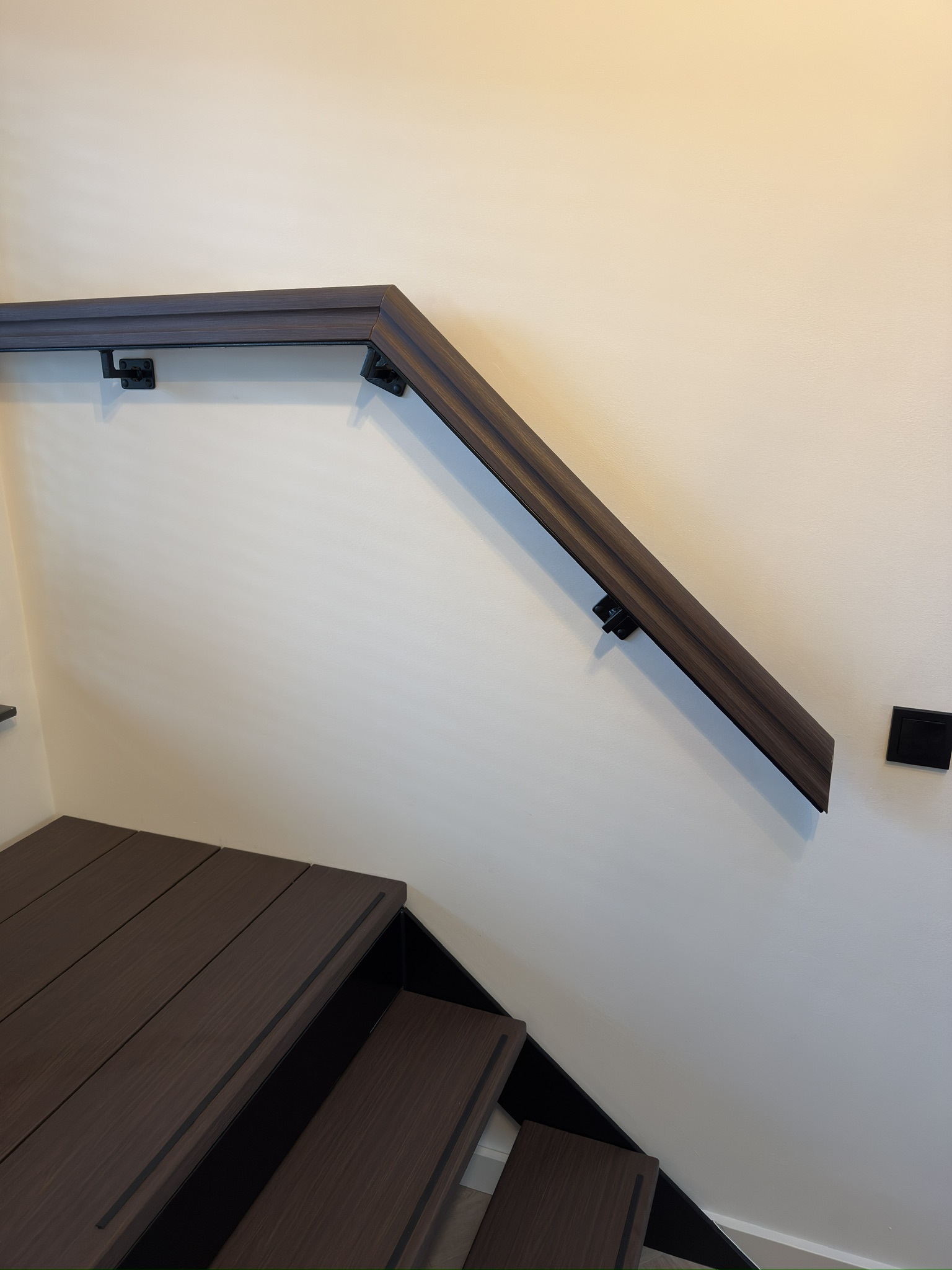 Wandleuning afgewerkt in dezelfde donkere houtlook als de trap